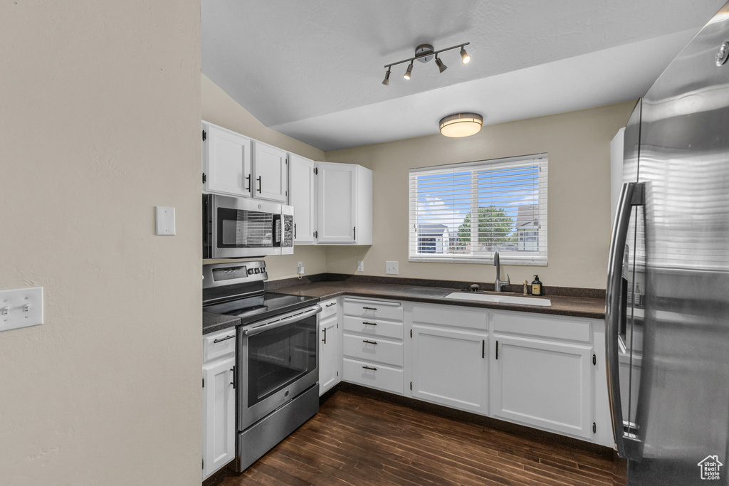 Kitchen featuring appliances with stainless steel finishes, a sink, dark countertops, dark wood-style flooring, and white cabinetry