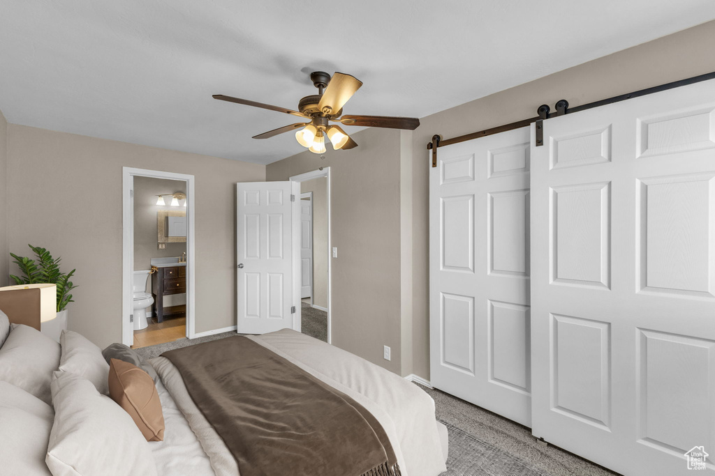 Bedroom with a barn door, ensuite bath, baseboards, ceiling fan, and light carpet