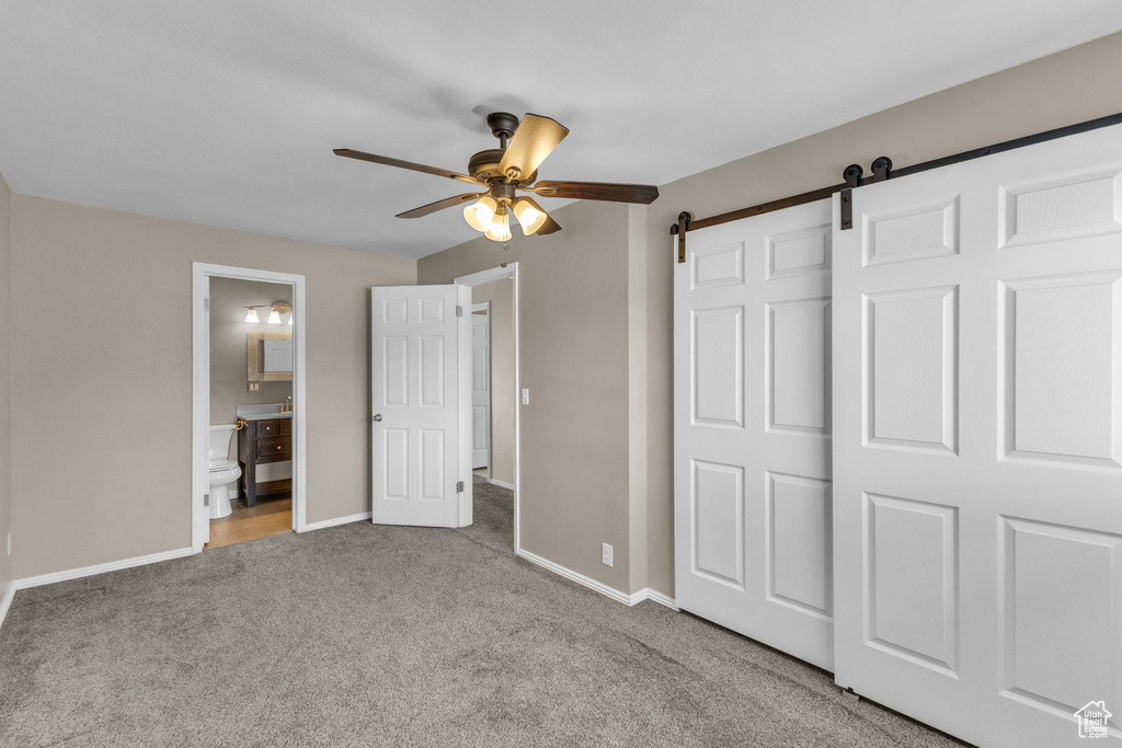 Unfurnished bedroom featuring carpet floors, baseboards, a barn door, and ensuite bathroom