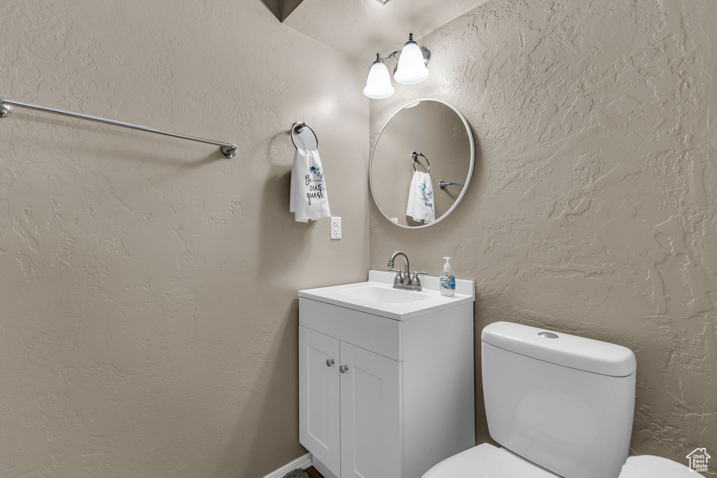 Half bath with vanity, toilet, and a textured wall