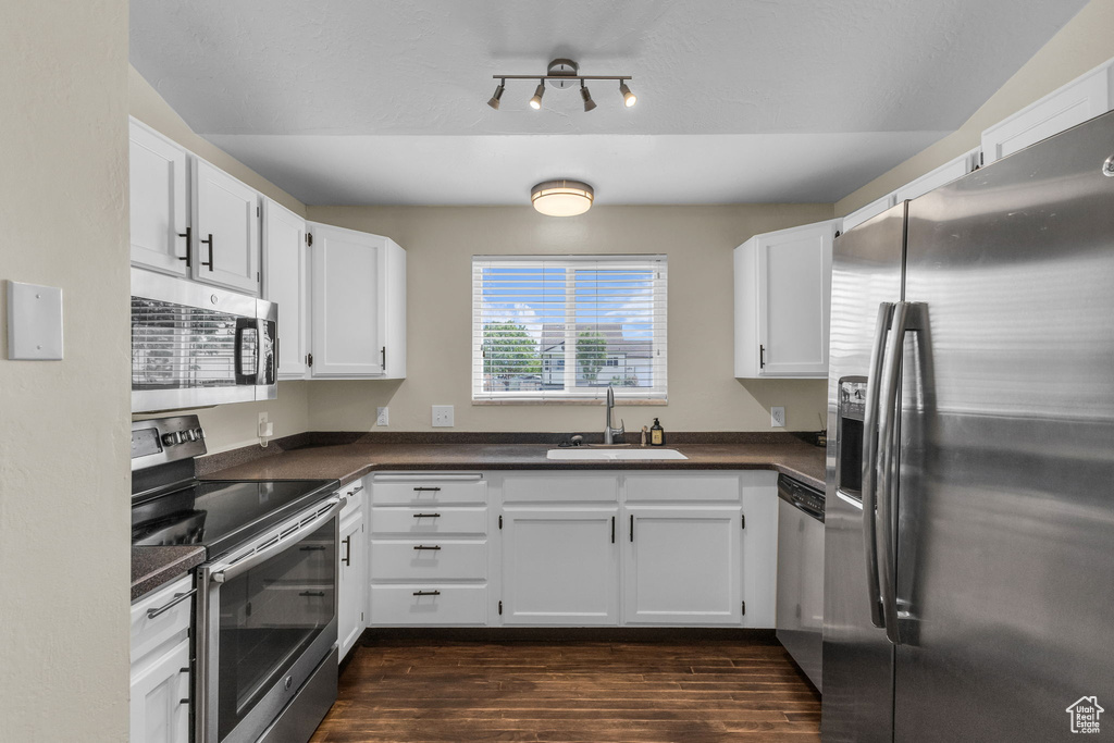 Kitchen featuring stainless steel appliances, a sink, dark countertops, white cabinetry, and dark wood-style flooring