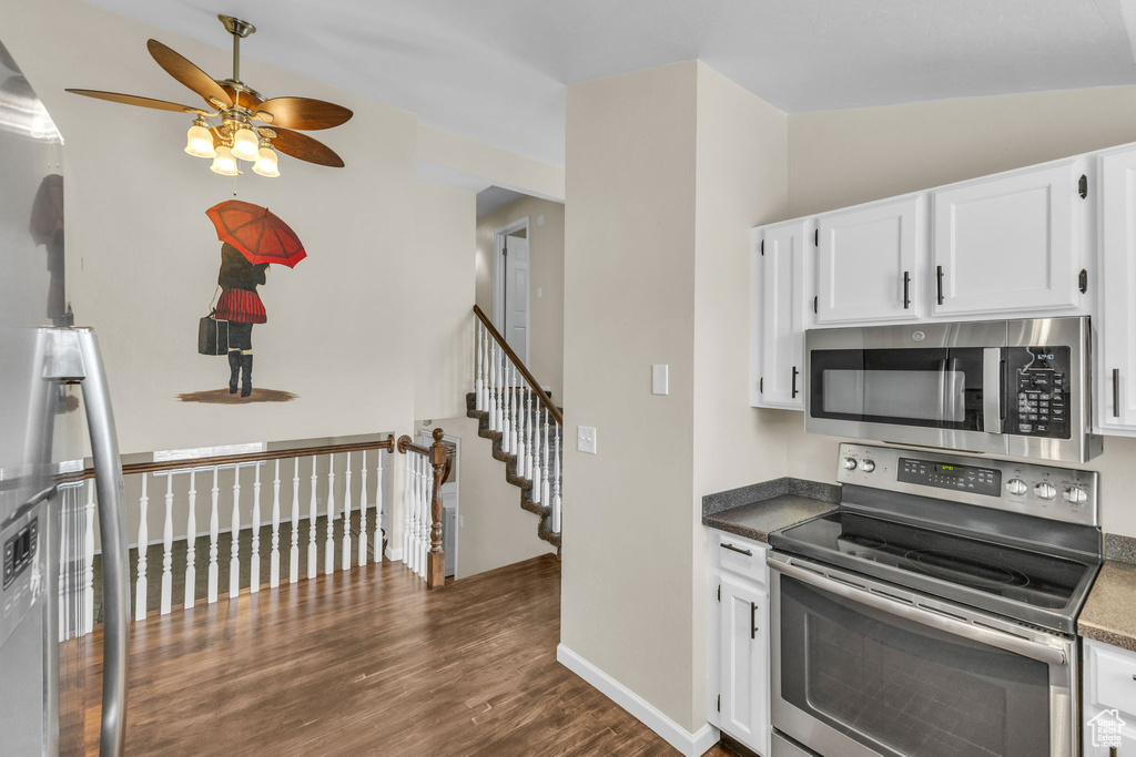 Kitchen with stainless steel appliances, ceiling fan, dark wood-style floors, white cabinetry, and baseboards