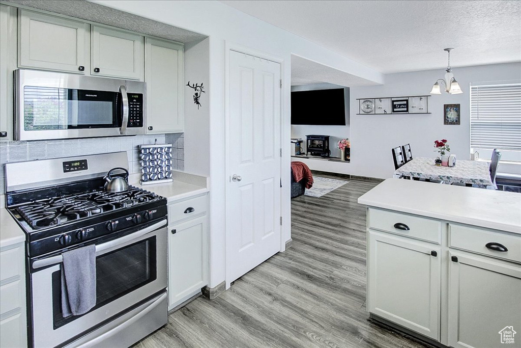 Kitchen with stainless steel appliances, light countertops, a chandelier, light wood-type flooring, and tasteful backsplash