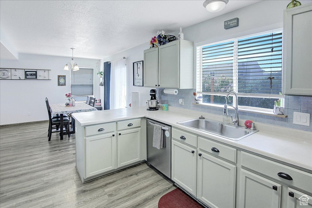 Kitchen featuring stainless steel dishwasher, a sink, a peninsula, light countertops, and a textured ceiling