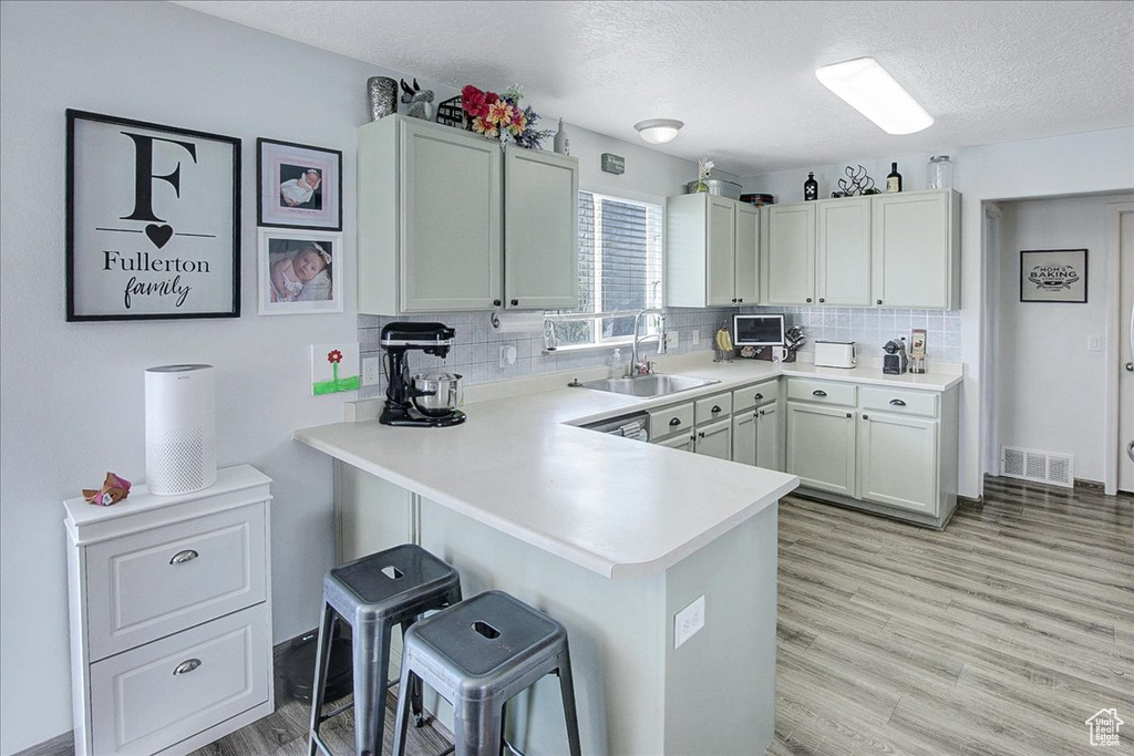 Kitchen with a sink, a kitchen breakfast bar, light countertops, light wood-type flooring, and backsplash