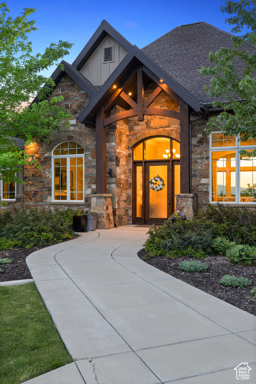Doorway to property featuring stone siding, board and batten siding, and a shingled roof
