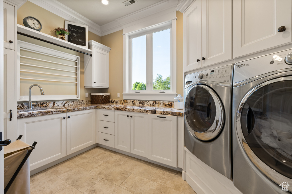 Washroom with cabinet space, washing machine and dryer, crown molding, and light tile patterned floors