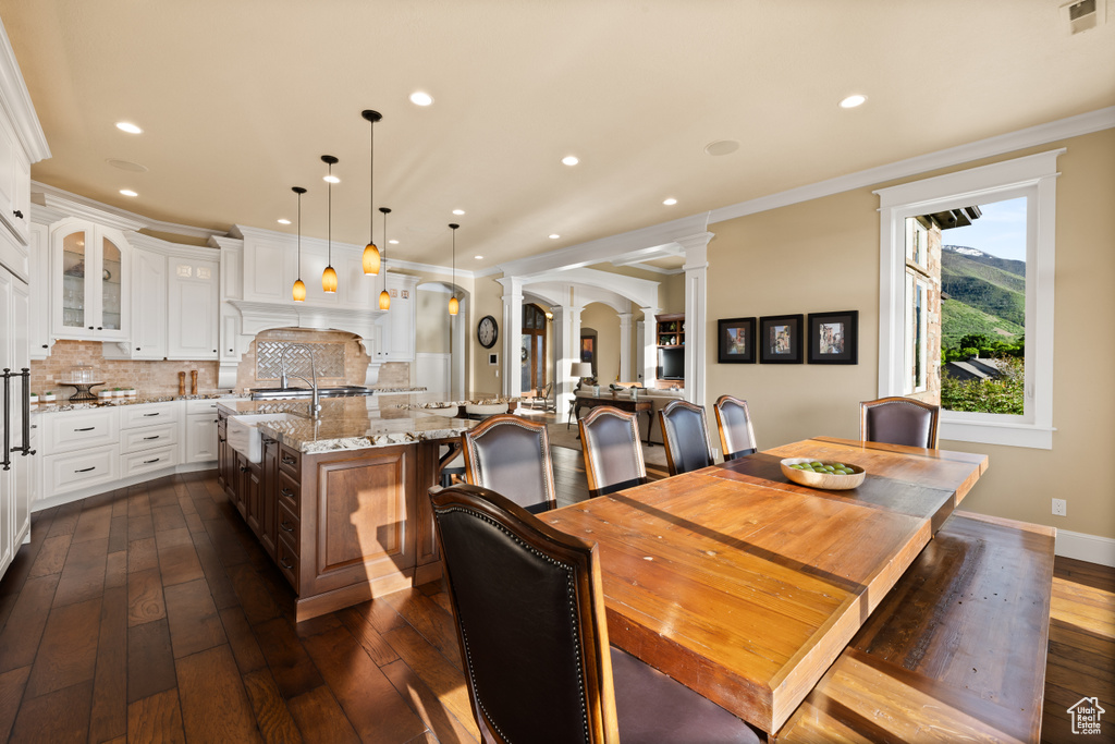 Dining room with decorative columns, arched walkways, dark wood-style flooring, recessed lighting, and crown molding