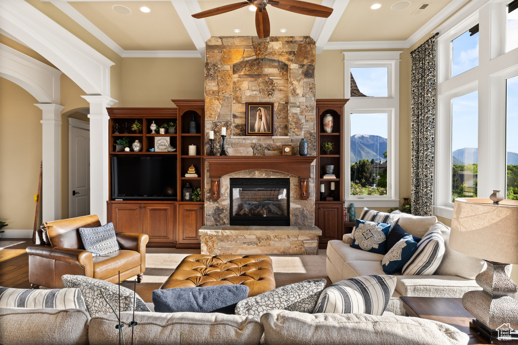 Living room featuring ornate columns, beamed ceiling, ceiling fan, a fireplace, and ornamental molding