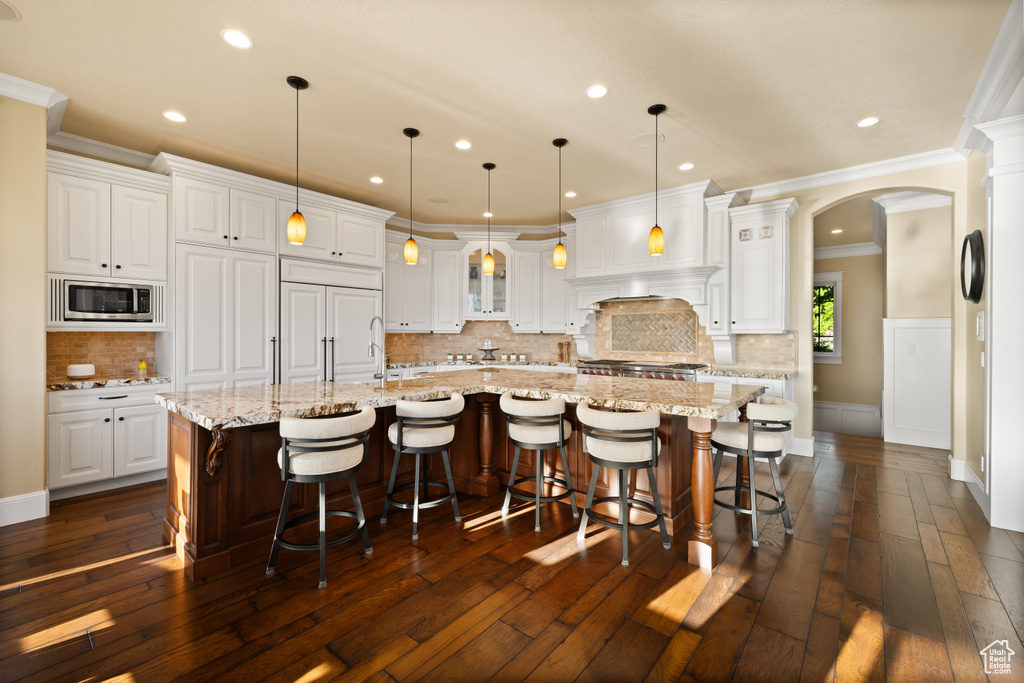 Kitchen with stainless steel microwave, ornamental molding, arched walkways, white cabinets, and a large island