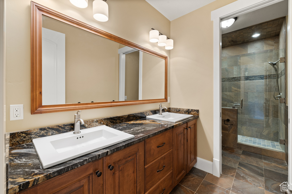 Full bathroom featuring a stall shower, double vanity, baseboards, and stone finish flooring