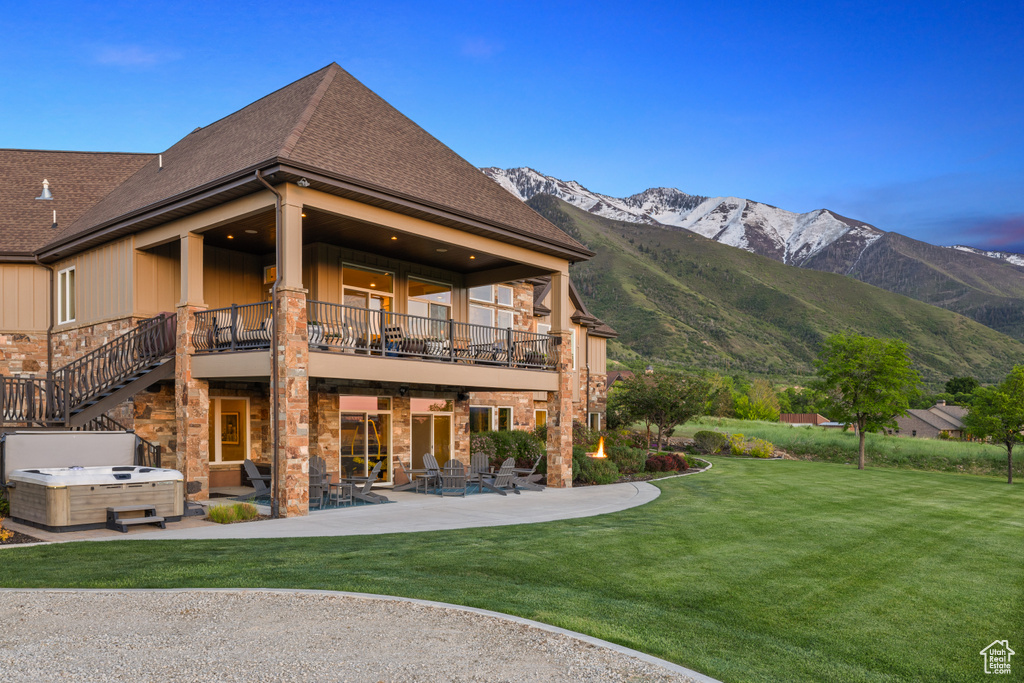 Rear view of property with a hot tub, a patio, a balcony, a lawn, and a mountain view