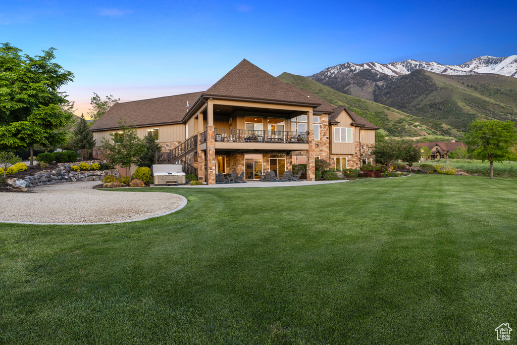 Rear view of property featuring a yard, stone siding, a mountain view, and a balcony