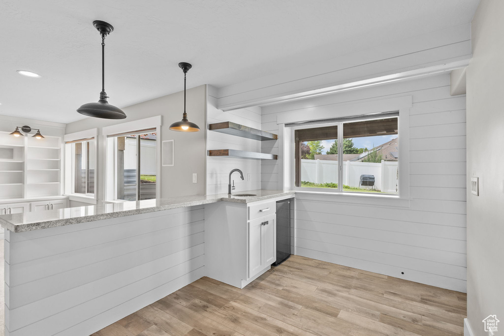Kitchen with a sink, a peninsula, open shelves, light stone counters, and white cabinetry