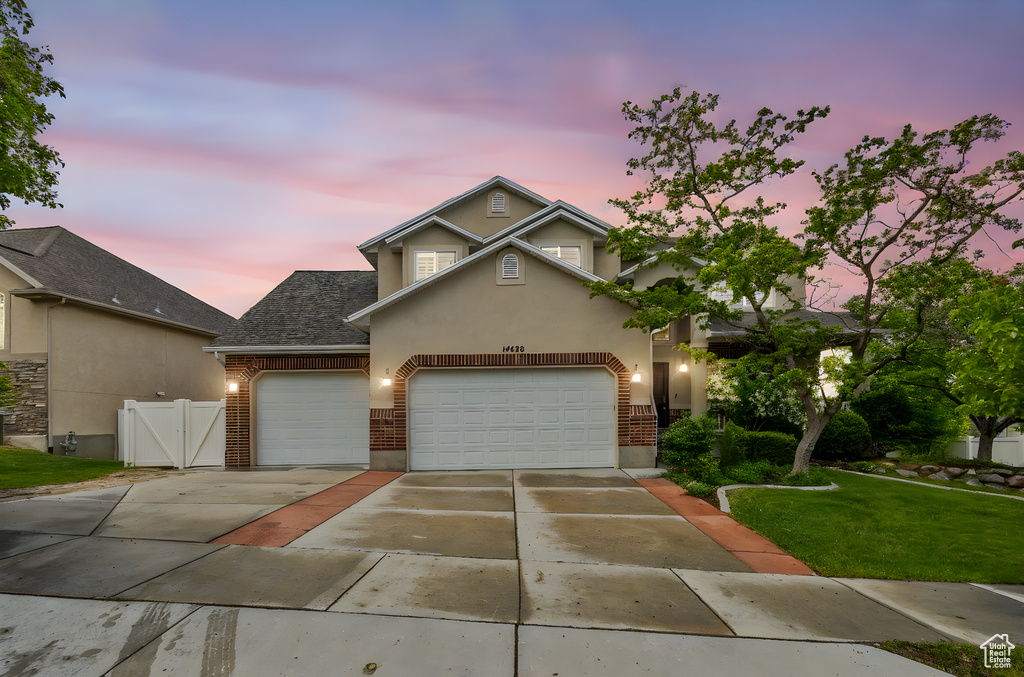 Traditional home with concrete driveway, brick siding, a garage, stucco siding, and a gate
