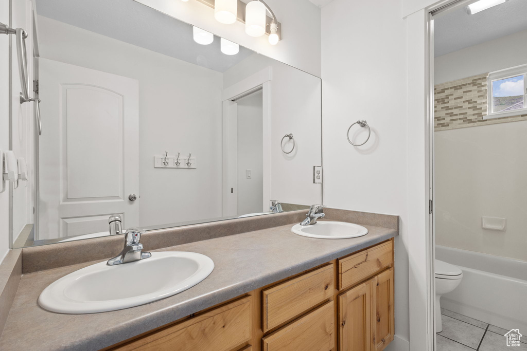 Full bathroom with double vanity, toilet, tile patterned floors, and shower / bath combination