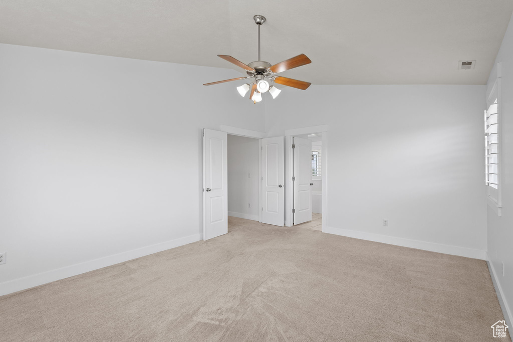 Empty room with a ceiling fan, lofted ceiling, light colored carpet, and baseboards