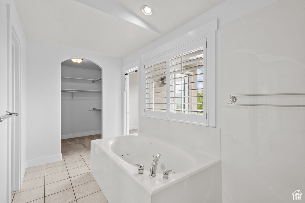 Full bathroom with a whirlpool tub, a walk in closet, tile patterned flooring, and baseboards