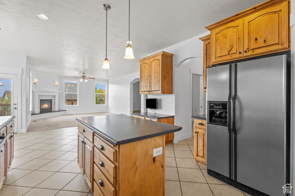 Kitchen with stainless steel refrigerator with ice dispenser, dark countertops, light tile patterned floors, arched walkways, and open floor plan