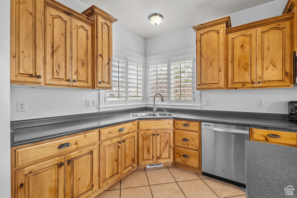 Kitchen with dishwasher, a sink, dark countertops, light tile patterned floors, and brown cabinetry