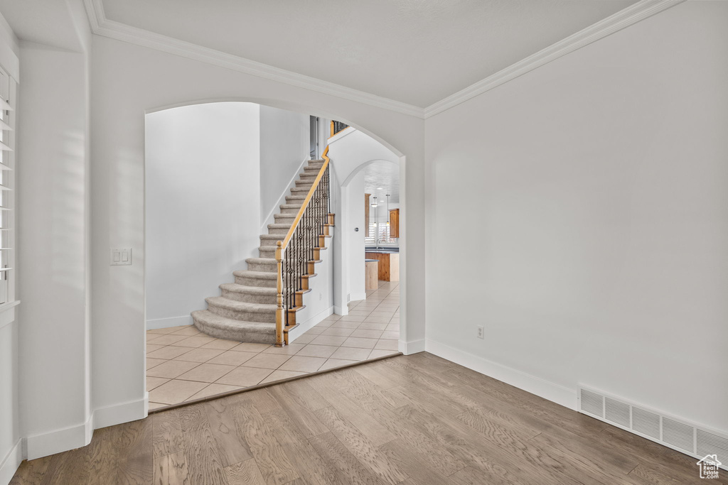 Spare room featuring arched walkways, crown molding, stairway, baseboards, and wood finished floors