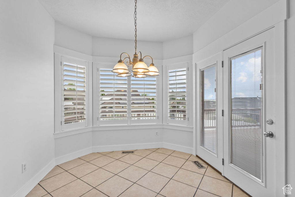 Unfurnished dining area featuring a chandelier, light tile patterned flooring, and baseboards