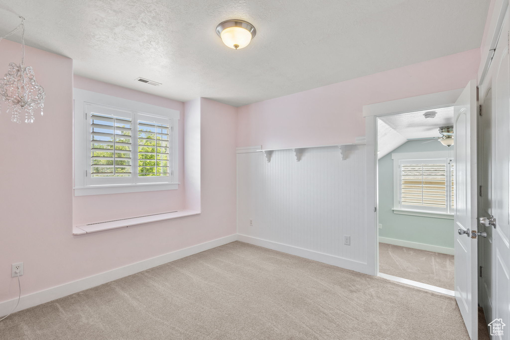 Empty room featuring light carpet, plenty of natural light, baseboards, a textured ceiling, and ceiling fan