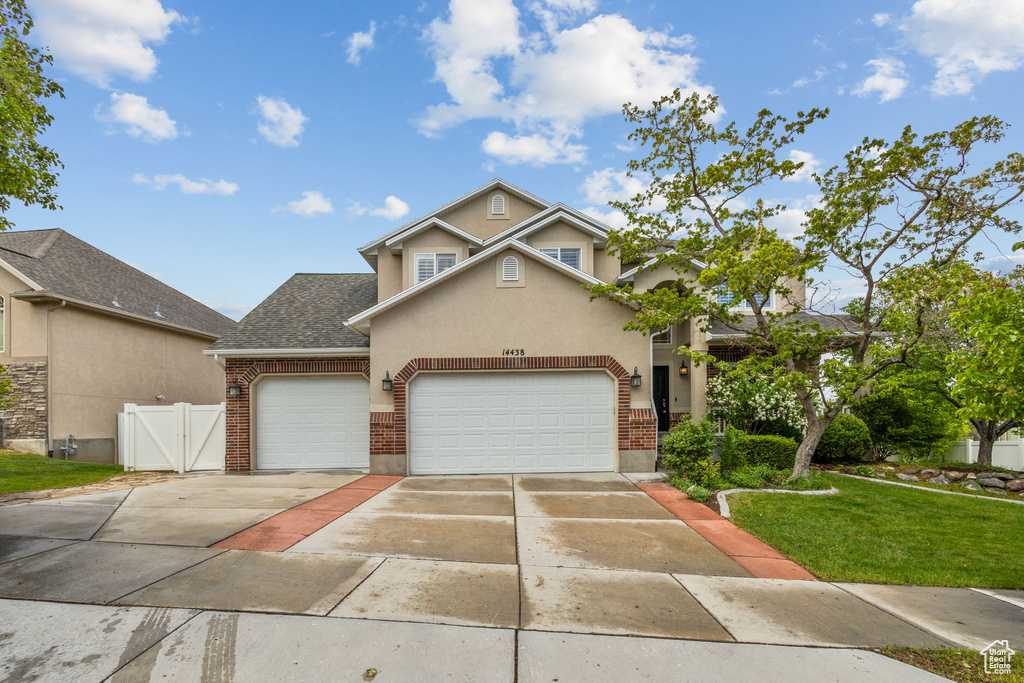 Traditional-style home with driveway, a garage, brick siding, stucco siding, and a gate