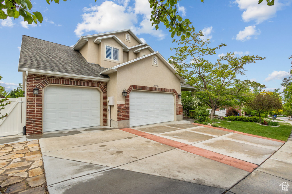 Traditional-style house with an attached garage, stucco siding, roof with shingles, driveway, and fence