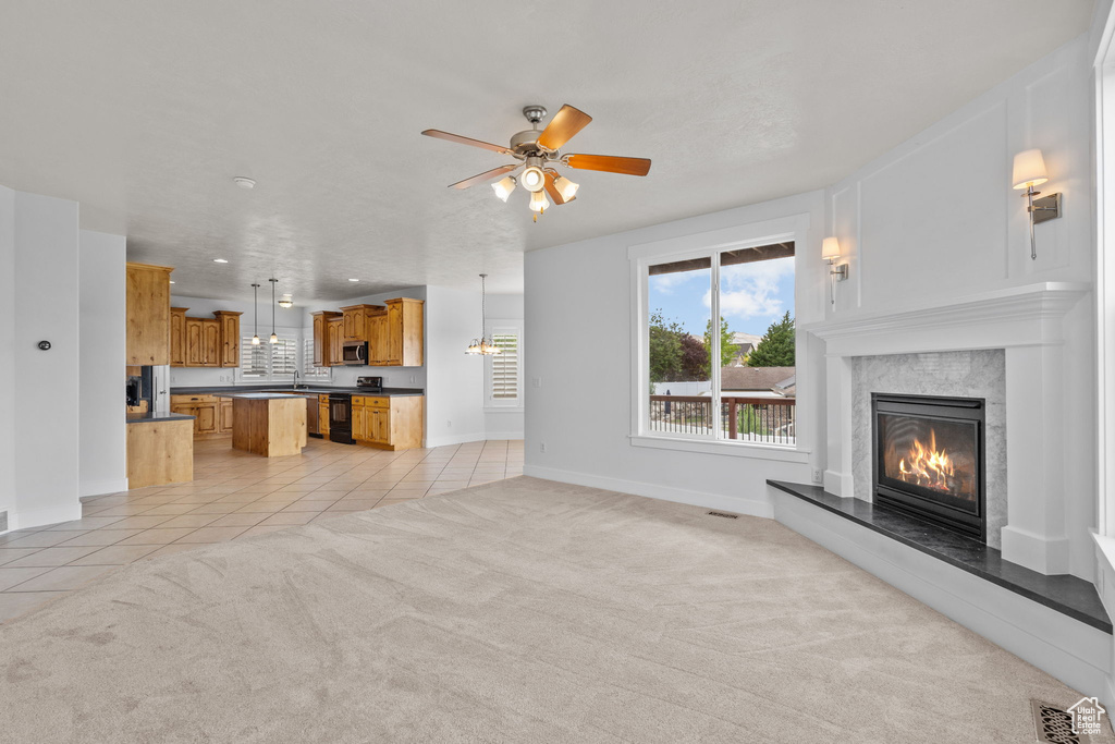 Unfurnished living room featuring a high end fireplace, light tile patterned floors, ceiling fan, light colored carpet, and baseboards