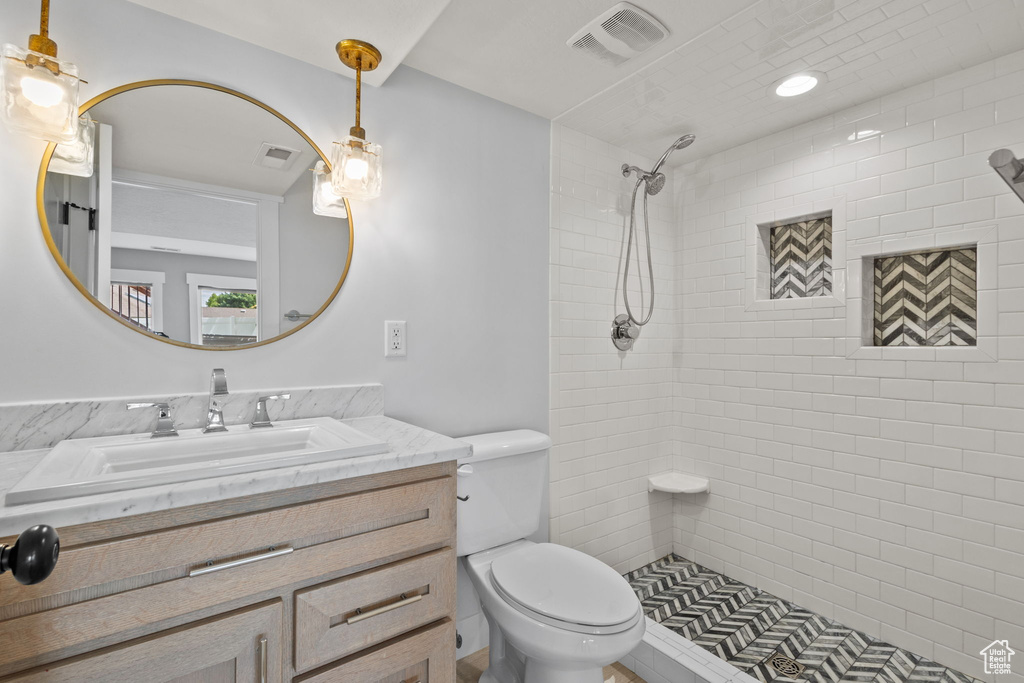 Full bath featuring toilet, tiled shower, and vanity