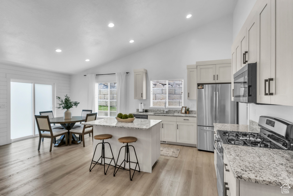 Kitchen featuring stainless steel appliances, vaulted ceiling, a kitchen breakfast bar, a center island, and a sink