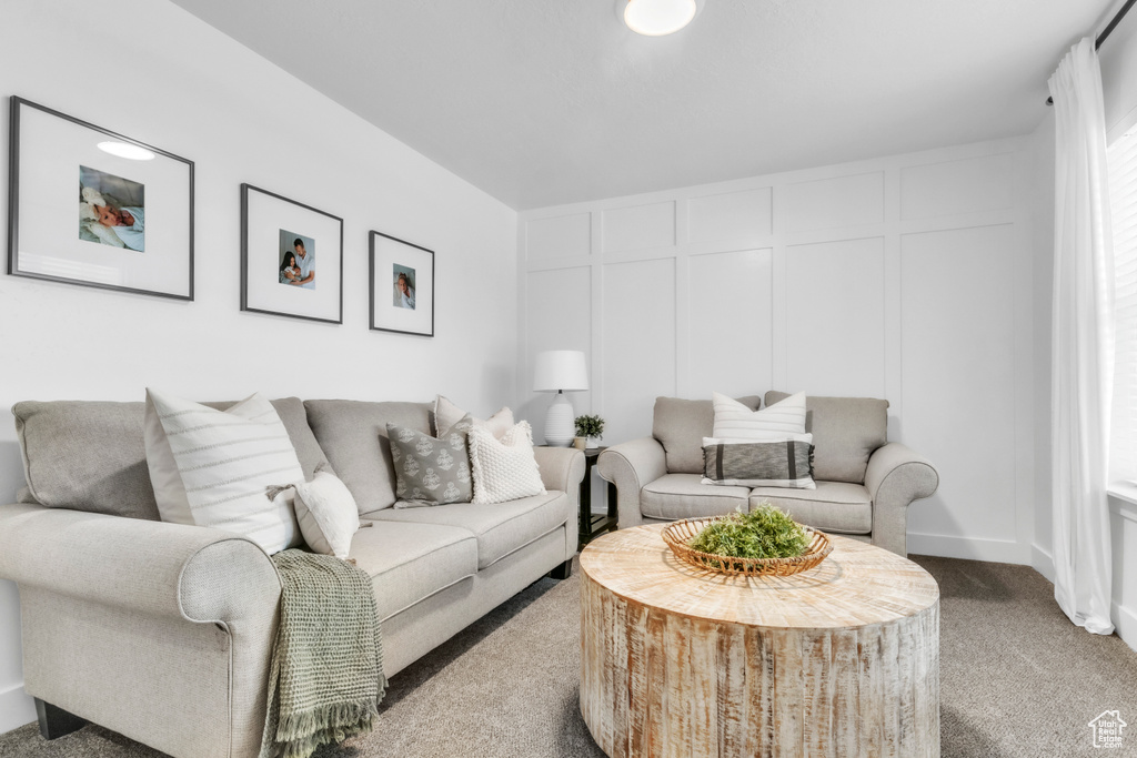 Living room featuring carpet flooring, a decorative wall, and baseboards