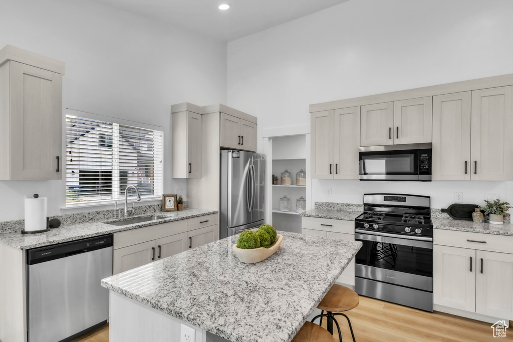 Kitchen with appliances with stainless steel finishes, a sink, a high ceiling, a kitchen bar, and a kitchen island