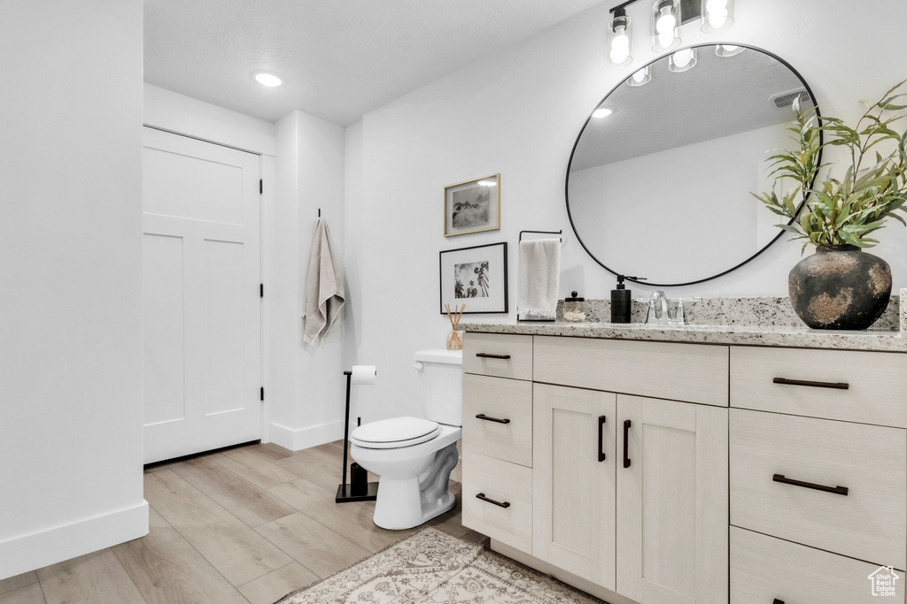 Bathroom with wood finished floors, toilet, vanity, baseboards, and recessed lighting