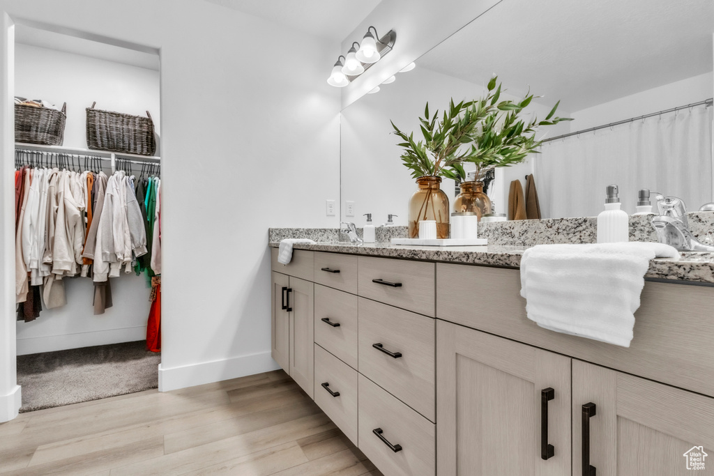 Bathroom with double vanity, wood finished floors, baseboards, and a walk in closet