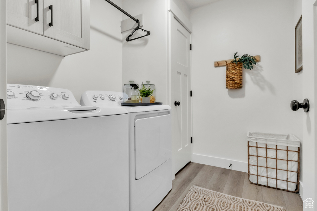 Laundry room with separate washer and dryer, cabinet space, light wood-style flooring, and baseboards