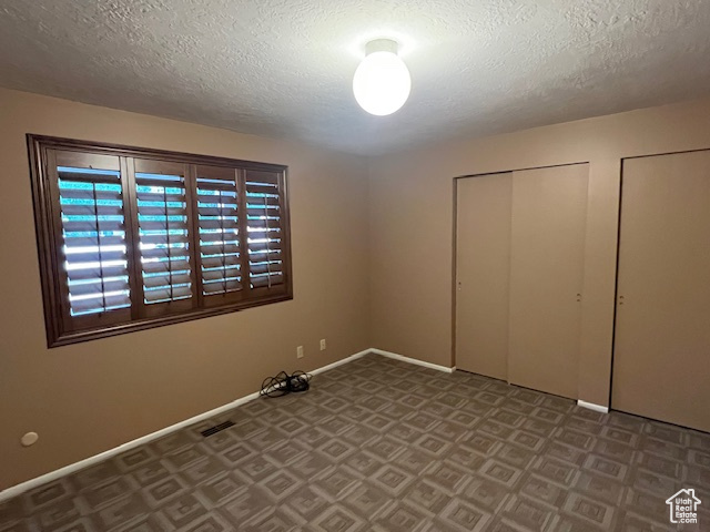 Unfurnished bedroom featuring a textured ceiling, baseboards, and multiple closets