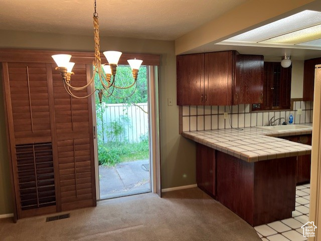 Kitchen featuring tile countertops, a chandelier, light carpet, and decorative backsplash