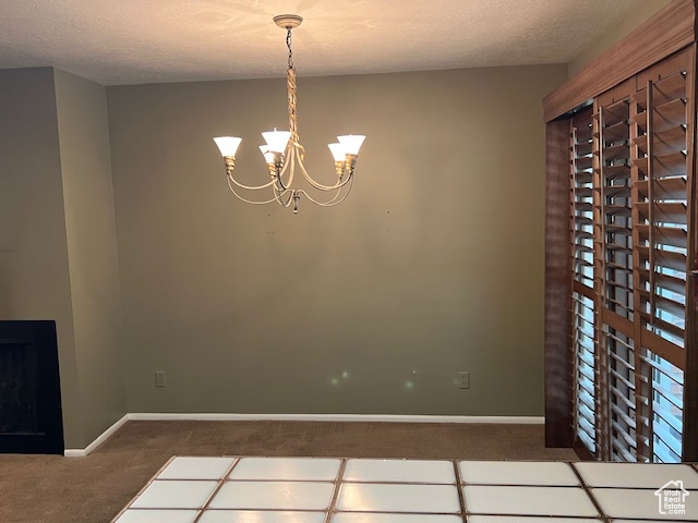 Unfurnished dining area featuring carpet floors, baseboards, a chandelier, and a textured ceiling