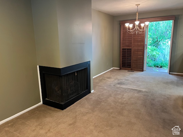 Unfurnished living room featuring carpet flooring, a chandelier, and baseboards
