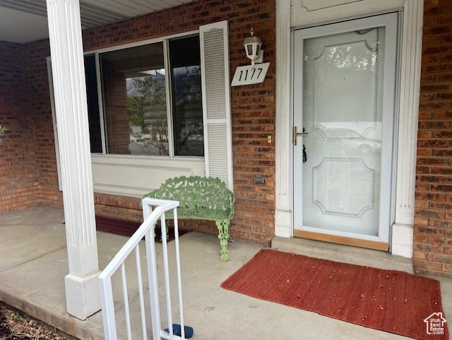 Doorway to property featuring brick siding and a porch