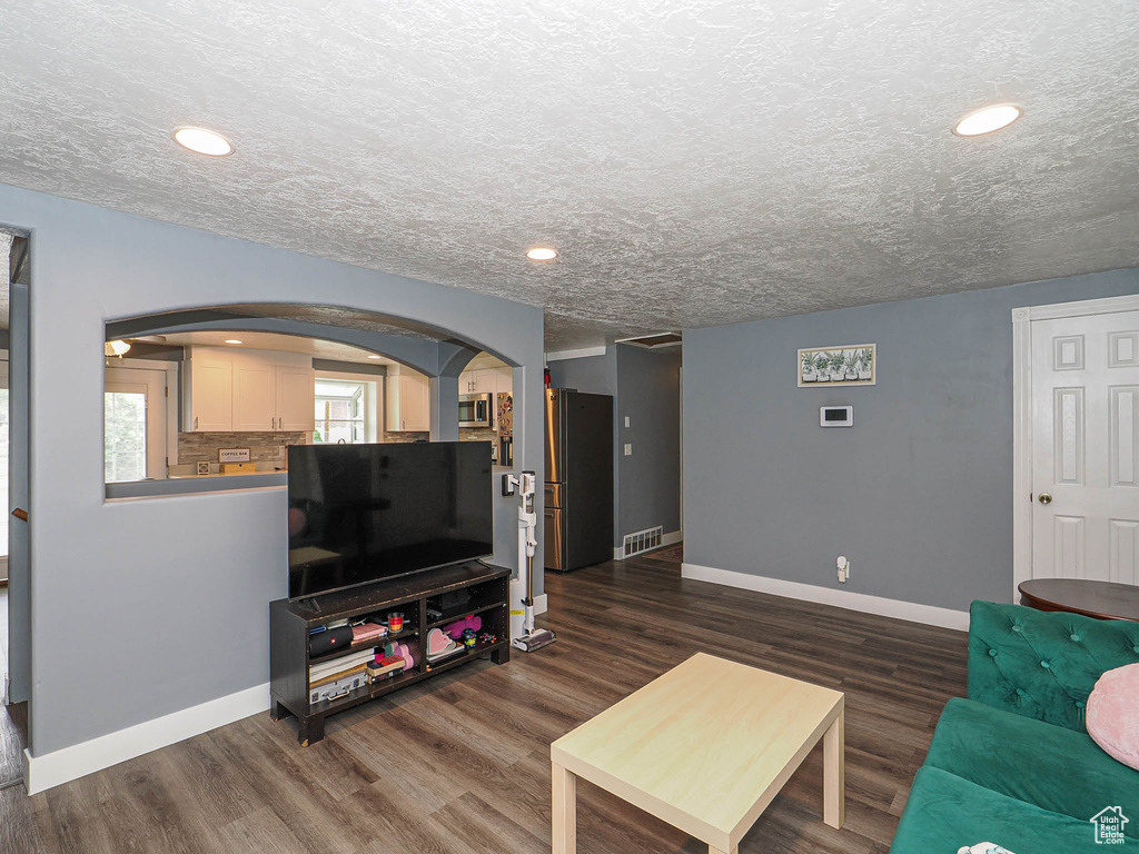Living area with arched walkways, baseboards, dark wood-type flooring, recessed lighting, and a textured ceiling