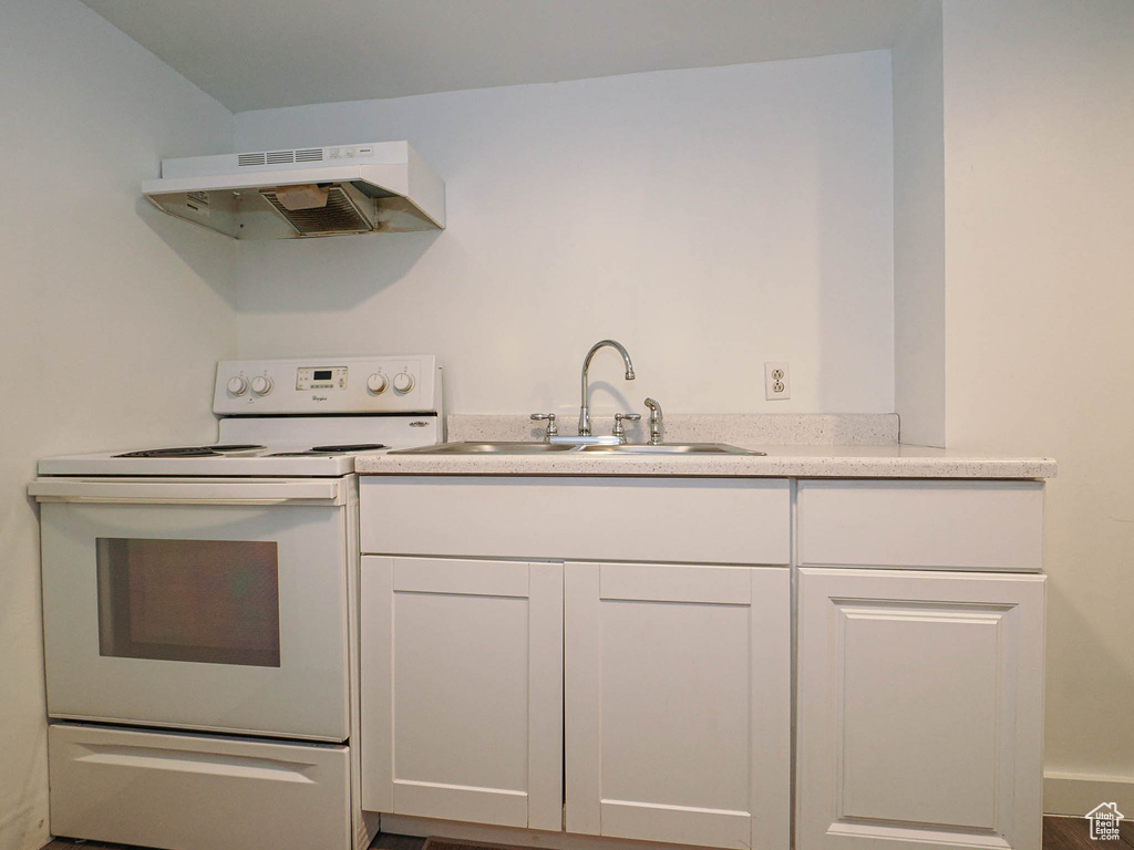 Kitchen with white range with electric stovetop, under cabinet range hood, a sink, and white cabinetry