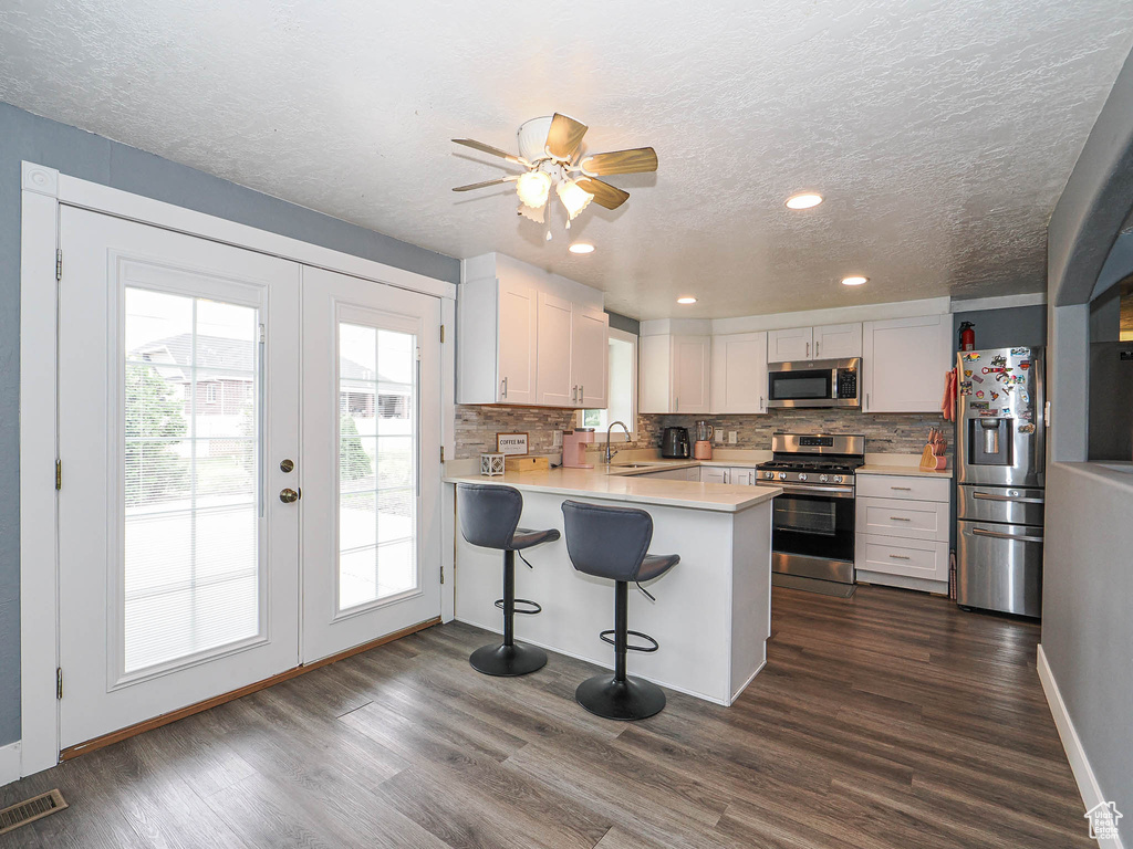 Kitchen with stainless steel appliances, french doors, light countertops, a peninsula, and backsplash