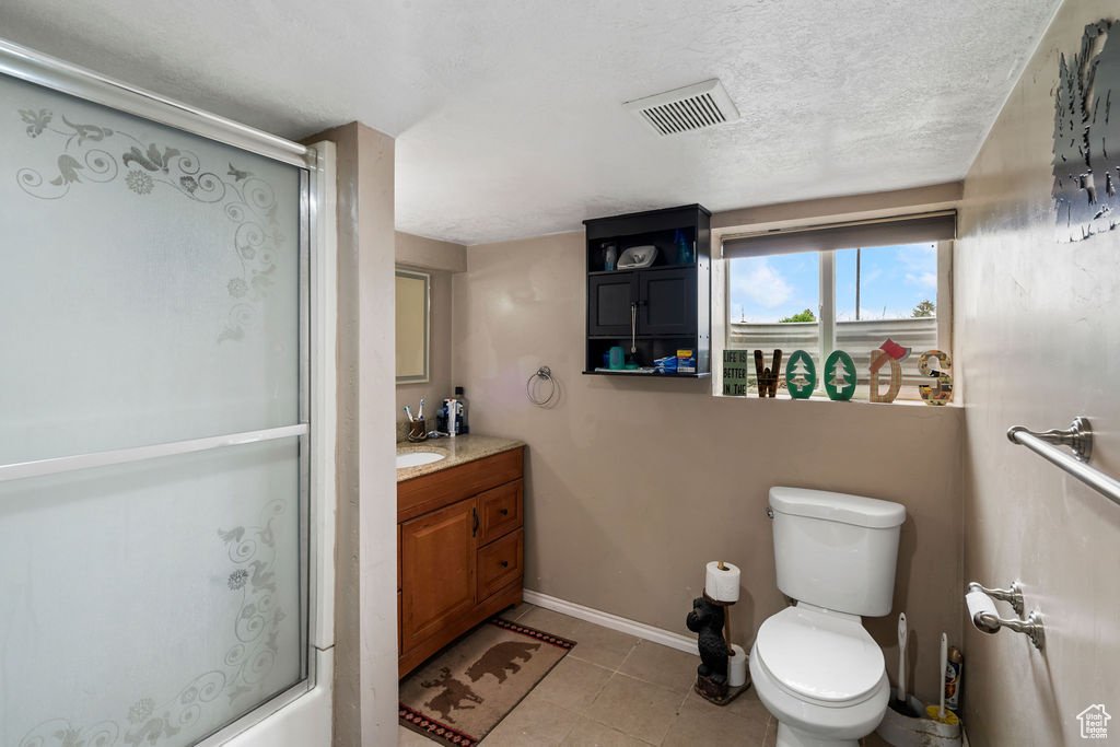 Full bathroom with an enclosed shower, tile patterned floors, baseboards, toilet, and a textured ceiling