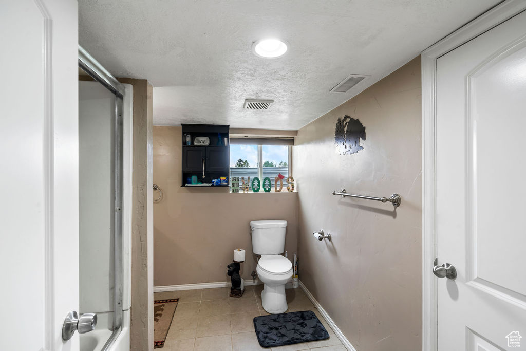 Bathroom with baseboards, a shower, toilet, tile patterned flooring, and a textured ceiling