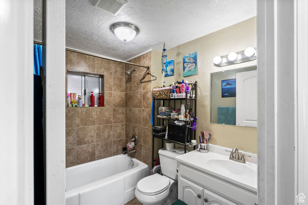 Bathroom featuring a textured ceiling,  shower combination, toilet, and vanity