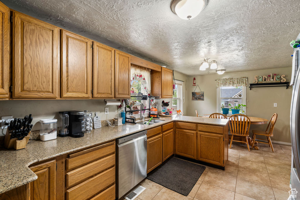 Kitchen with dishwasher, a sink, light countertops, a peninsula, and light tile patterned flooring