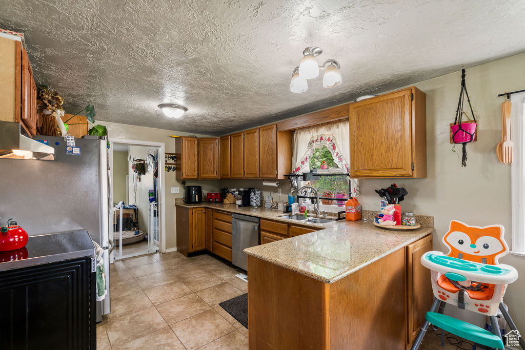 Kitchen featuring stainless steel appliances, a sink, a peninsula, brown cabinets, and a textured ceiling